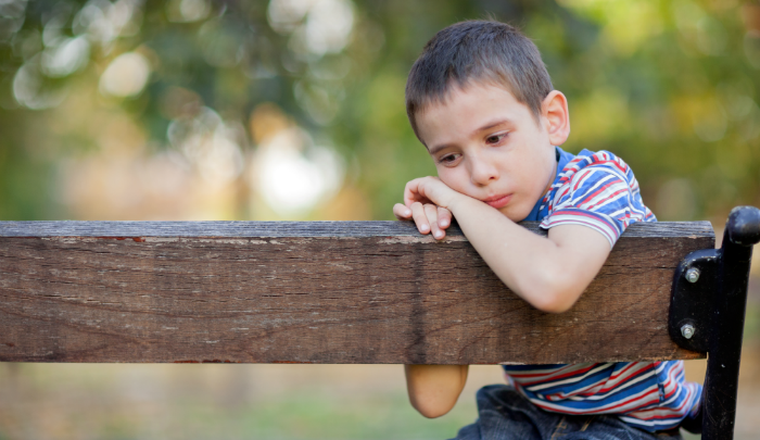 boy sitting on a wooden bench looking sad: parents, are you there but not really there?