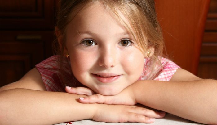 Small girl smiling and resting her head on her hands