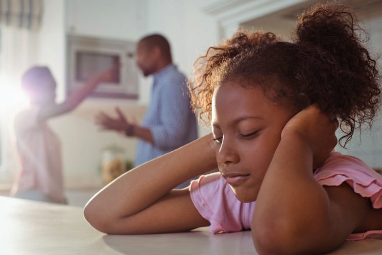 Child covering her ears while her parents are arguing in the background