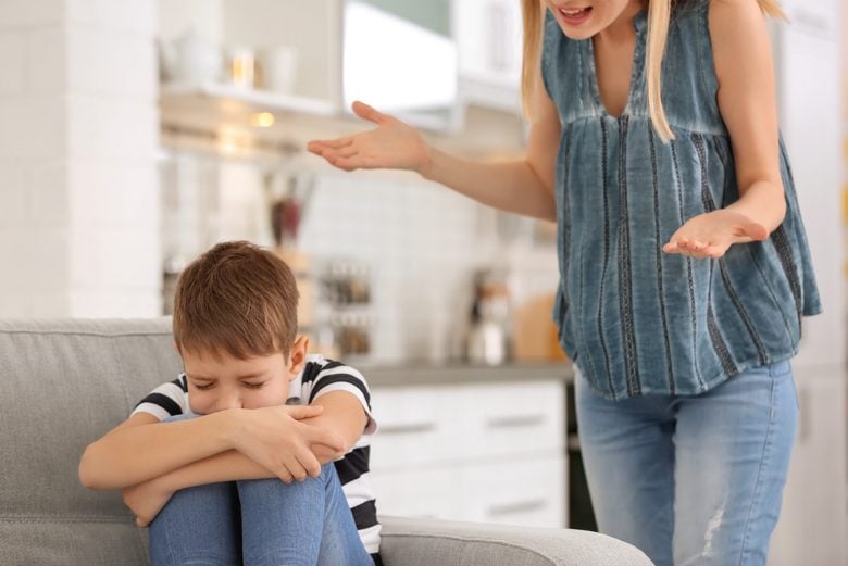 Sad child on a couch with a frustrated mother behind him