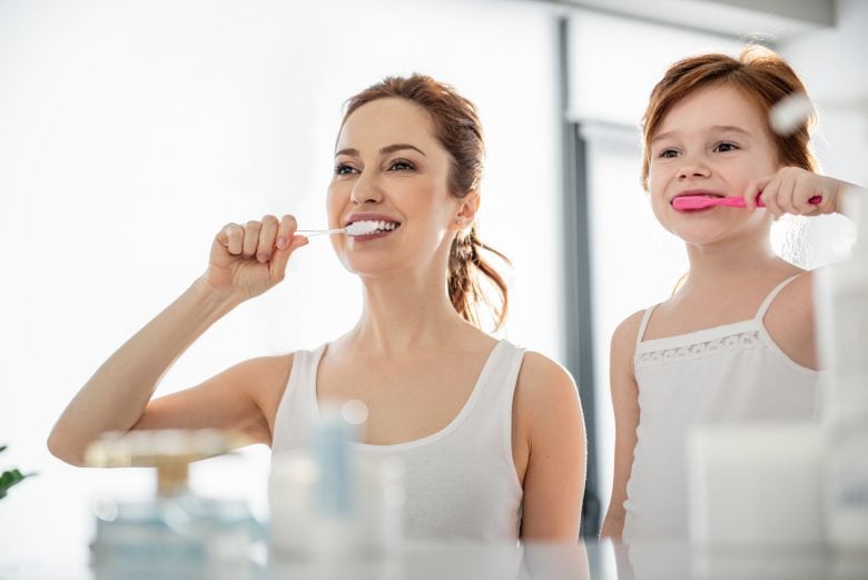 Mother and daughter looking in mirror brushing teeth