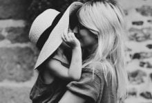 girl peeking out from a hat to kiss her mother