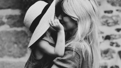 girl peeking out from a hat to kiss her mother